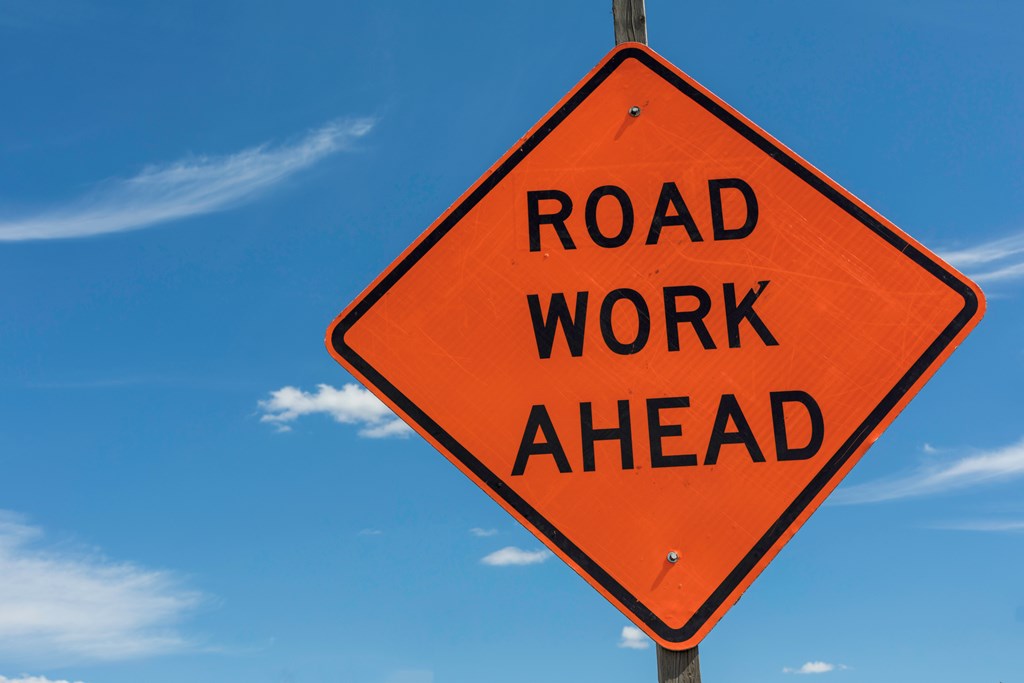 Road Work Ahead sign shown against a bright blue sky.