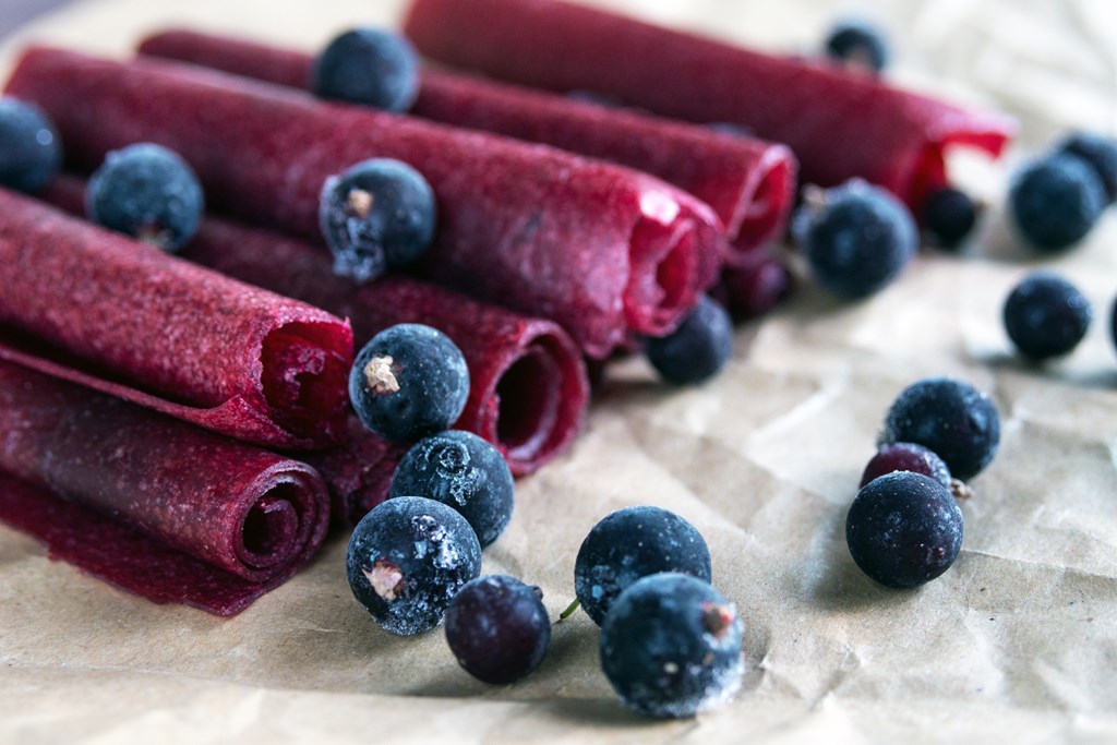 Handmade fruit leather in tight roles surrounded by blueberries.
