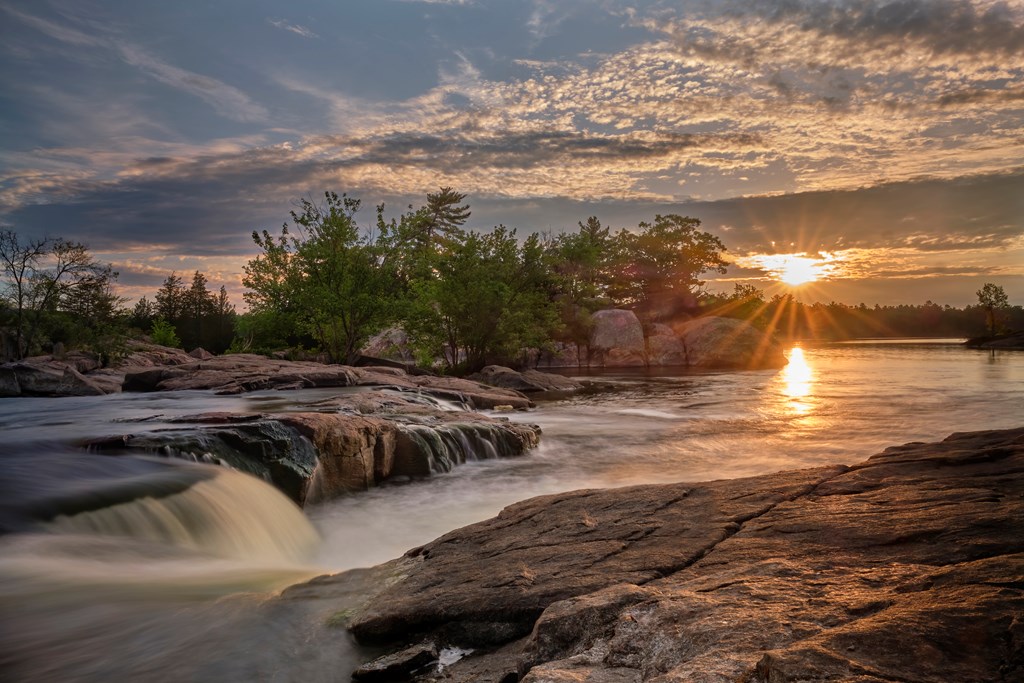 A beautiful sunrise at Burleigh Falls Ontario shows a starburst pattern of the sun with some colorful lens flare.