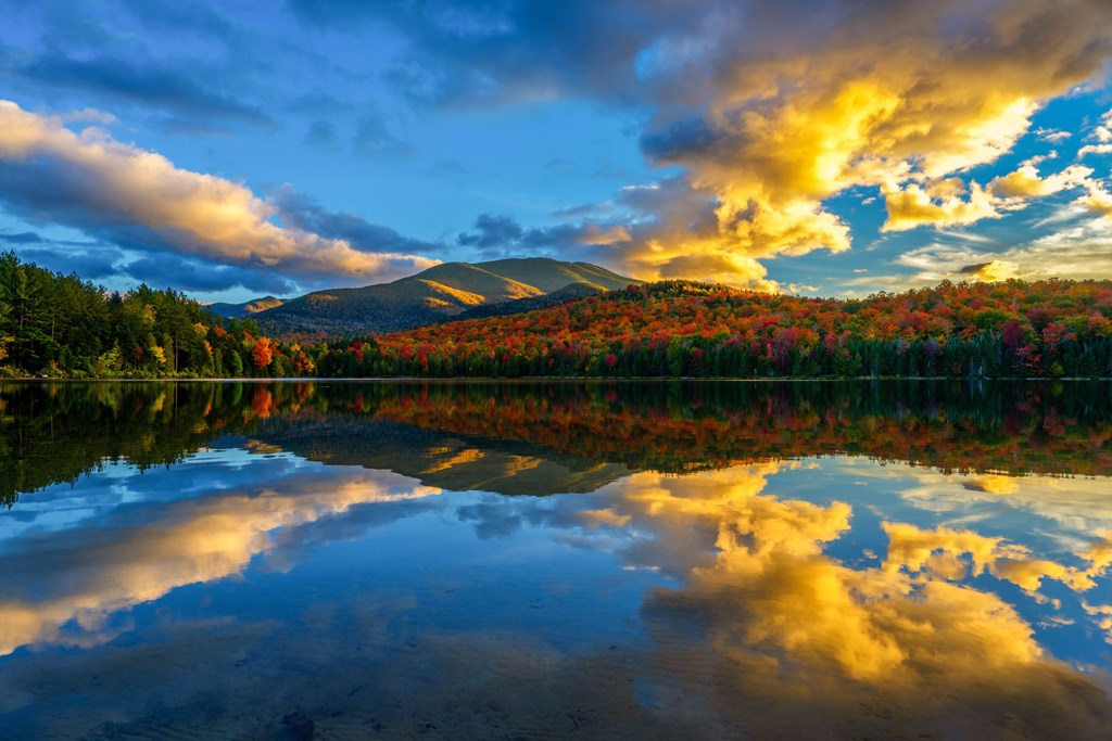 A scenic shot of the lake surrounded by fall forest against the Adirondack Mountains.