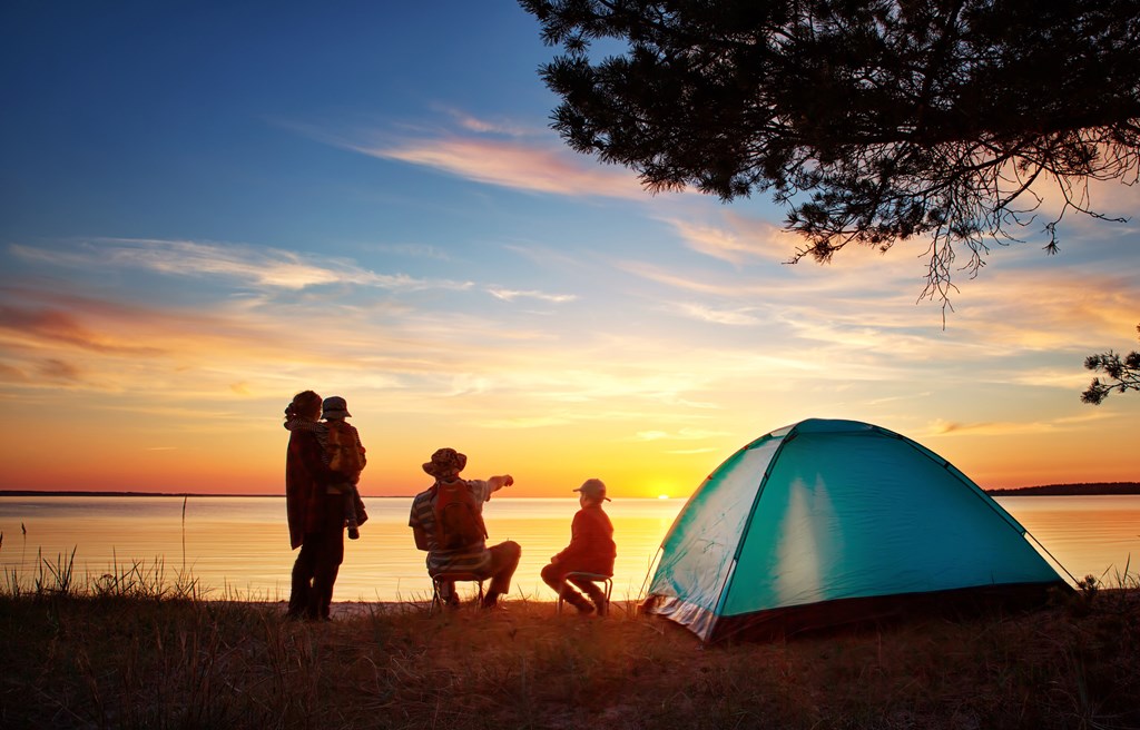 Family camping by a lake at sunset.