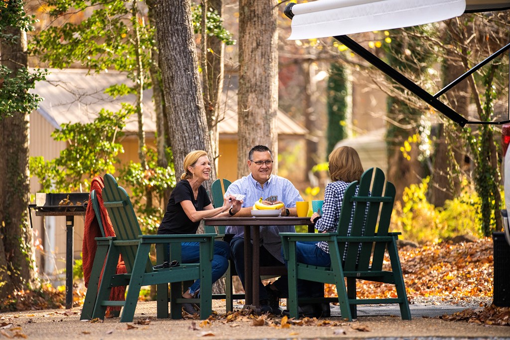 Three people sit around a table at a KOA campsite during the fall.