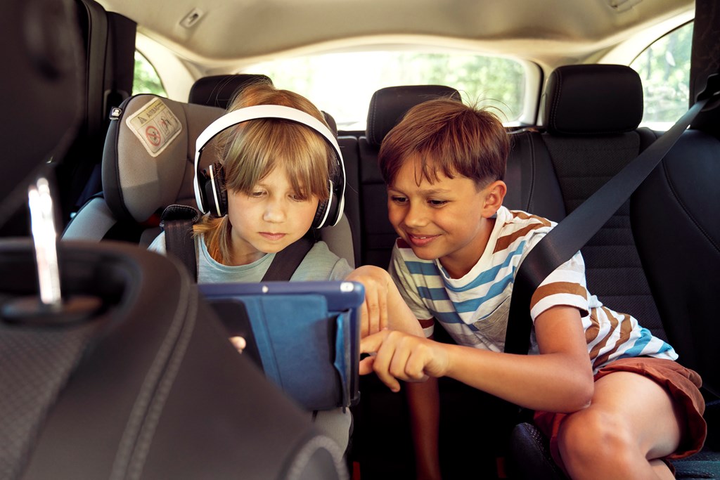 Little boy and little girl look at a tablet in the backseat on a road trip.