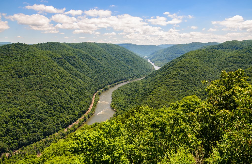 View of the New River Gorge National Park and Reserve from an overlook with green rolling mountains and a blue sky.