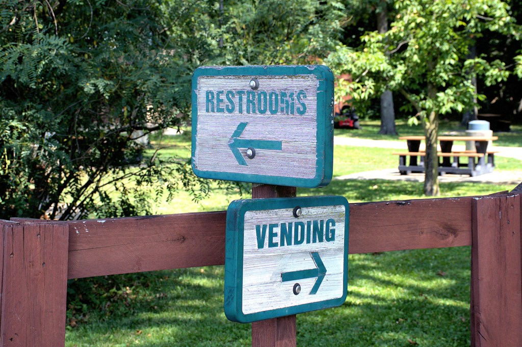Wooden signs posted in a highway rest stop park pointing the way to restrooms and vending machines.