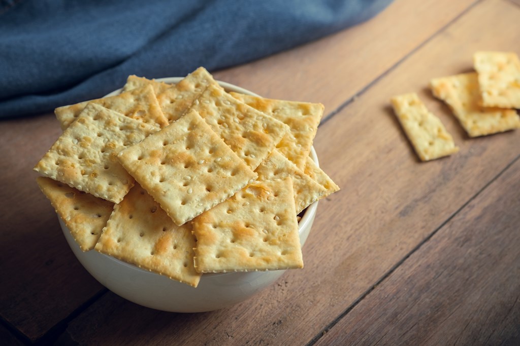 Saltine crackers in a bowl on a wooden background.
