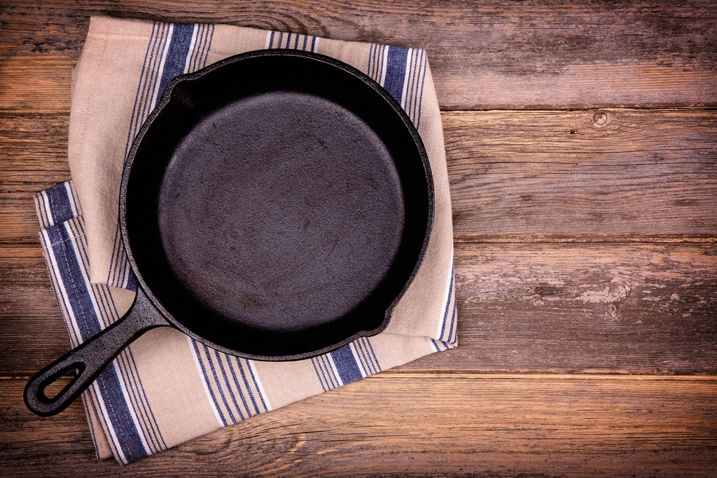 Empty cast iron skillet with tea towel, over old wood background. 