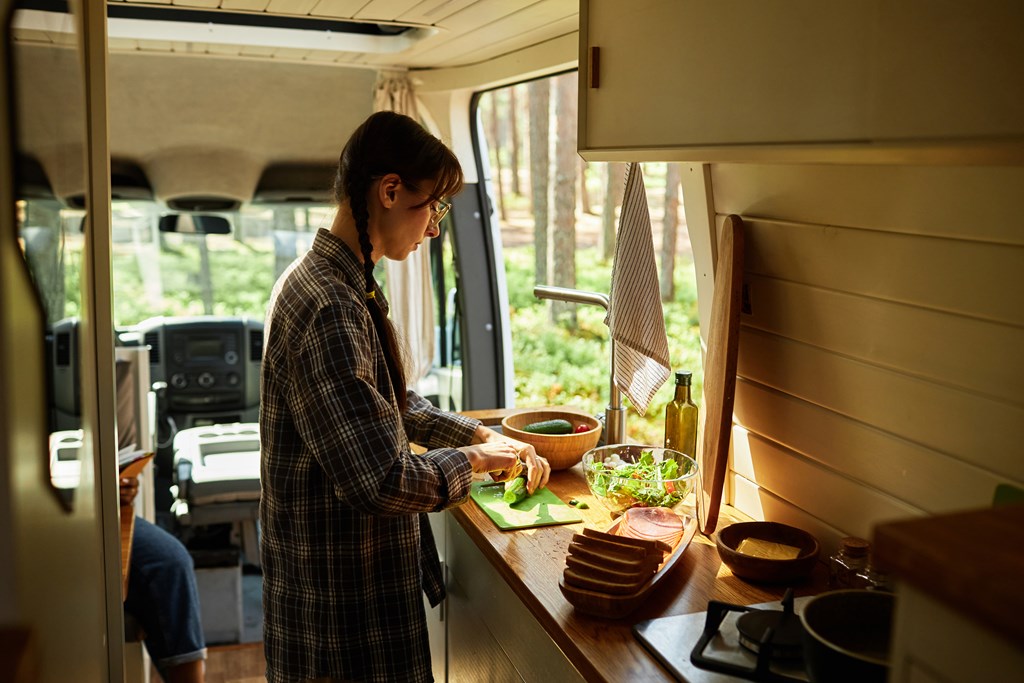 Young woman cutting vegetables on the counter of a camper van.