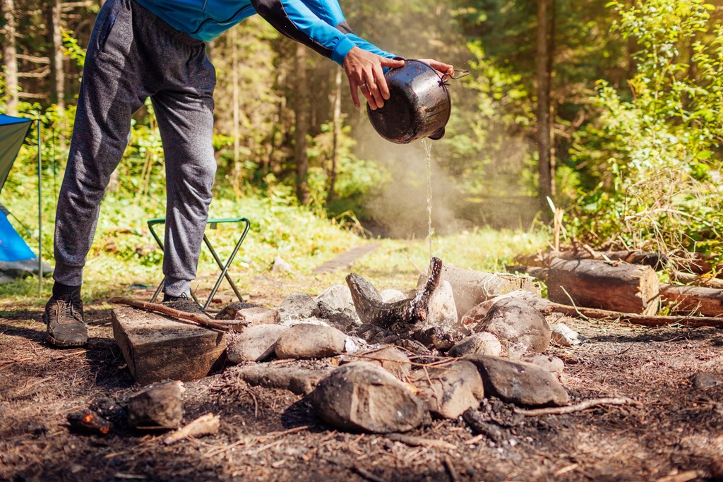 Man extinguishing campfire with water from a pot.