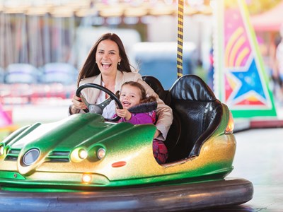A mom and her daughter are laughing and having fun while sitting inside of a bumper car at Belmont Park.