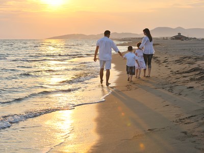 A family with two young children walk along the beach during sunset.
