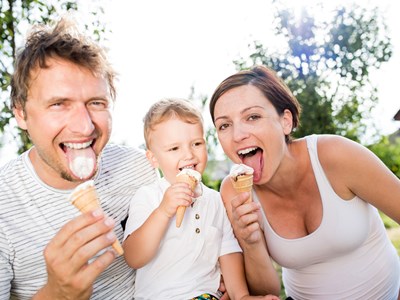 A family of three lick ice cream cones and laugh while enjoying a sunny day at Balboa Park.