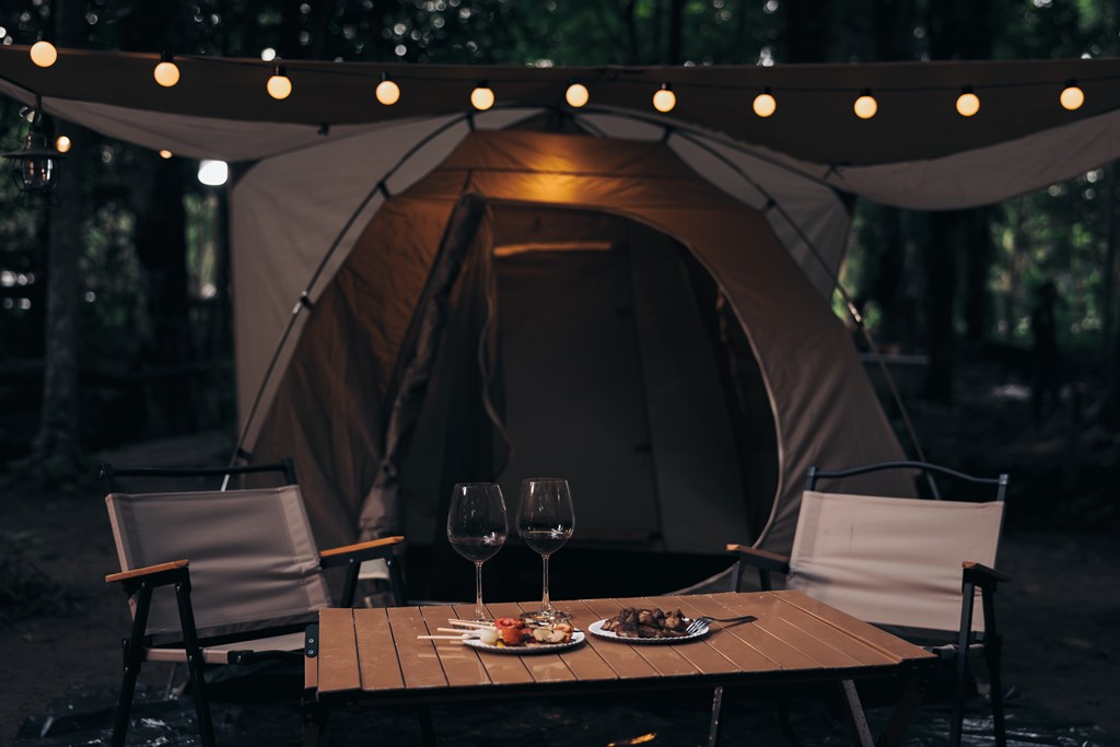 Closeup of two wine glasses in with a tent with string lights in the background at twilight. 
