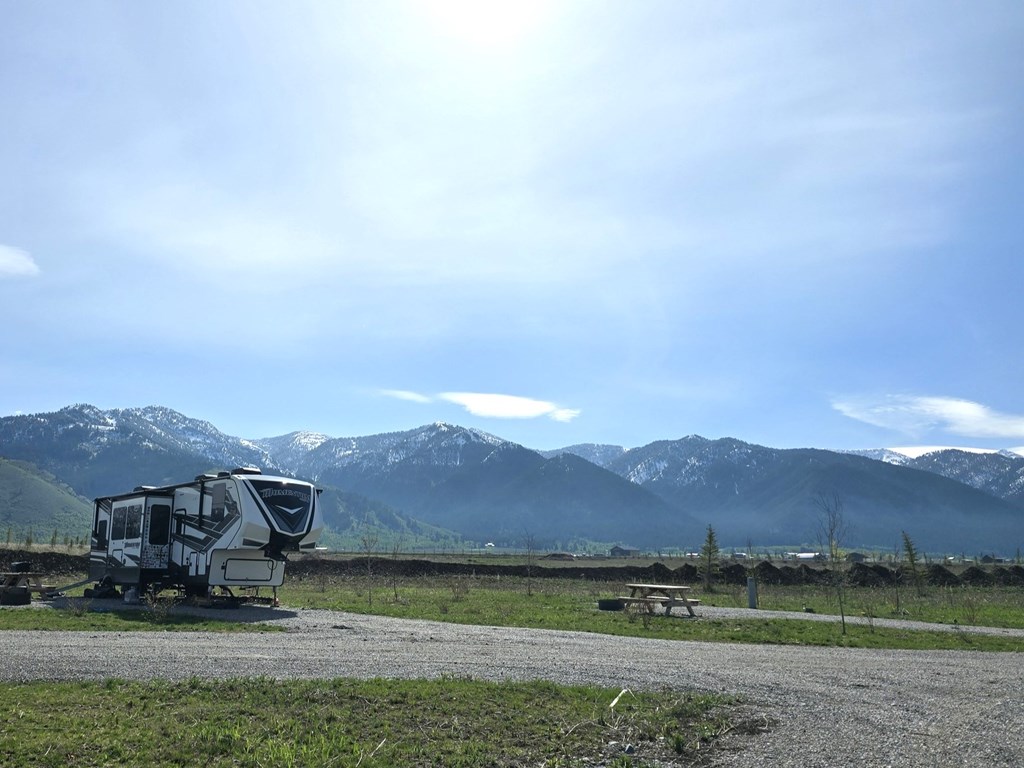 RV parked under blue sky with mountains in the background at Alpine Bridger Teton National Forest KOA Holiday