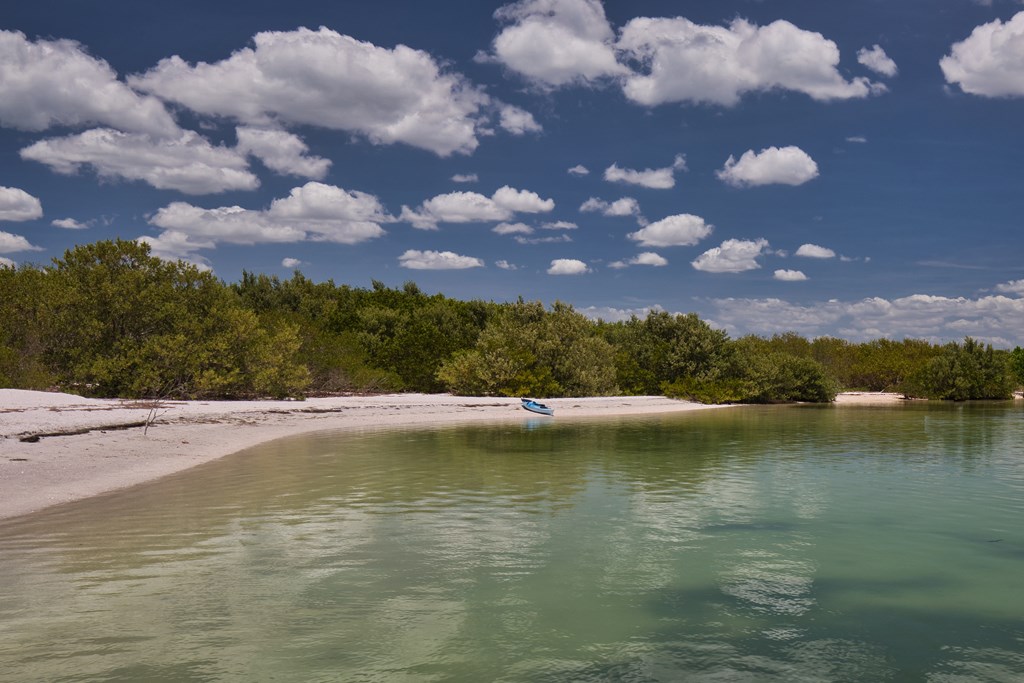 An empty kayak on a deserted beach along a cove with clear water and blue skies in Fort De Soto Park in St. Petersburg, FL.