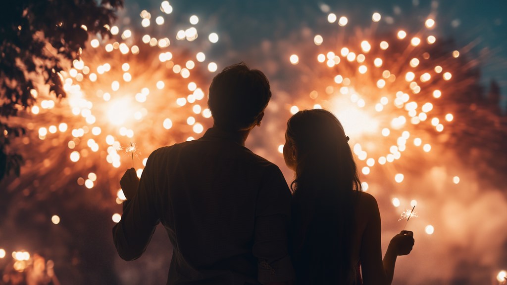 Couple watches fireworks while holding sparklers at night