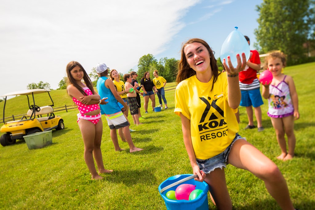 Young KOA campground employee in a yellow shirt runs a water activity for kids.