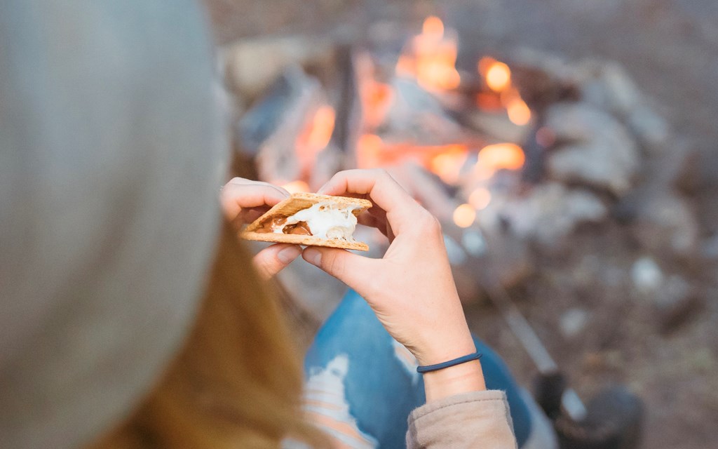 Closeup of a woman holding a s'more in front of a campfire.