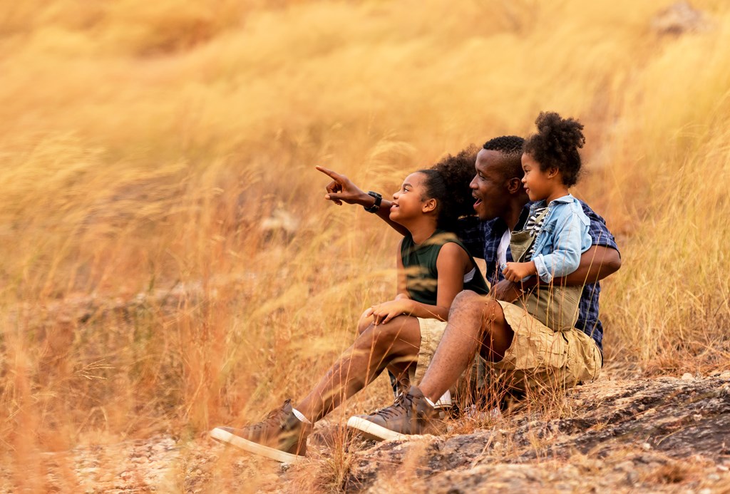 Father and two young daughters sit on a hill enjoying nature.