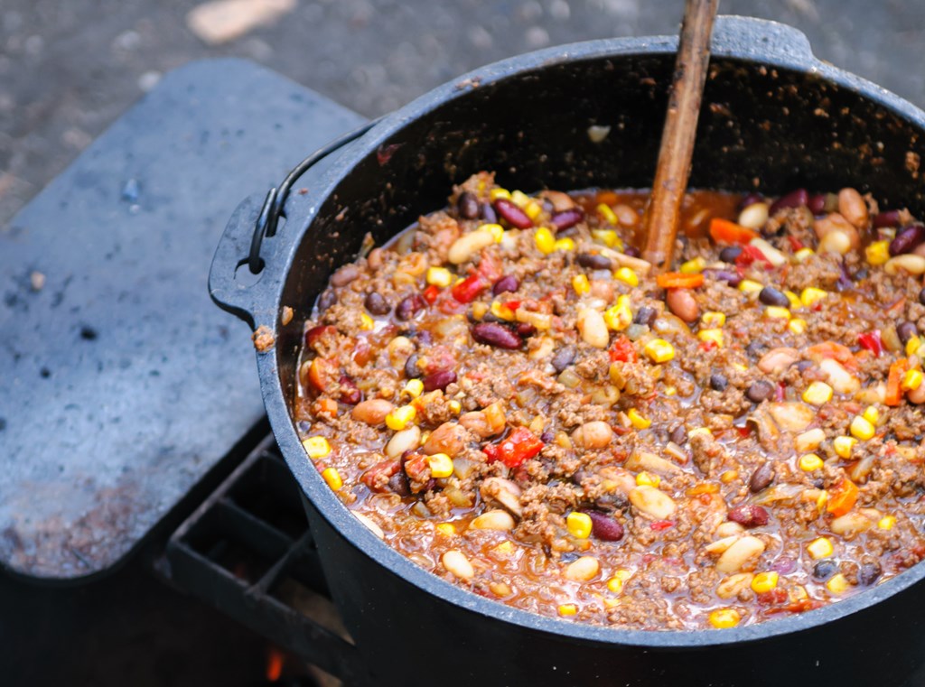 Large cast iron pot of spicy chili cooking over a campfire.