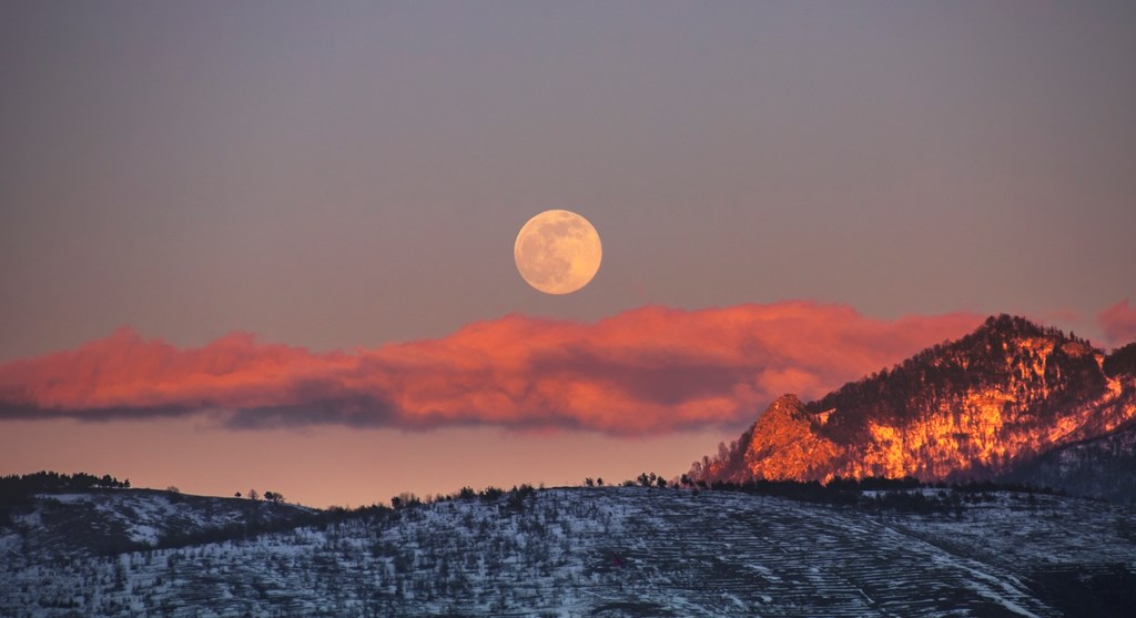 Full moon rising over a winter landscape in late afternoon.