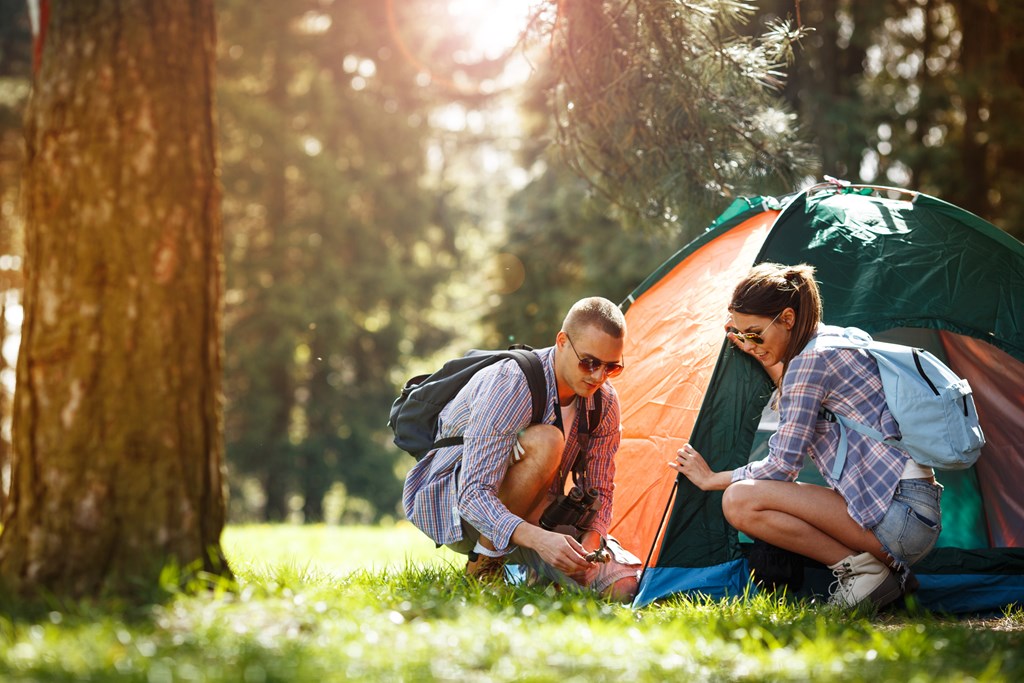 Two campers, a man and a woman, setting up the tent in a forest in the summer.