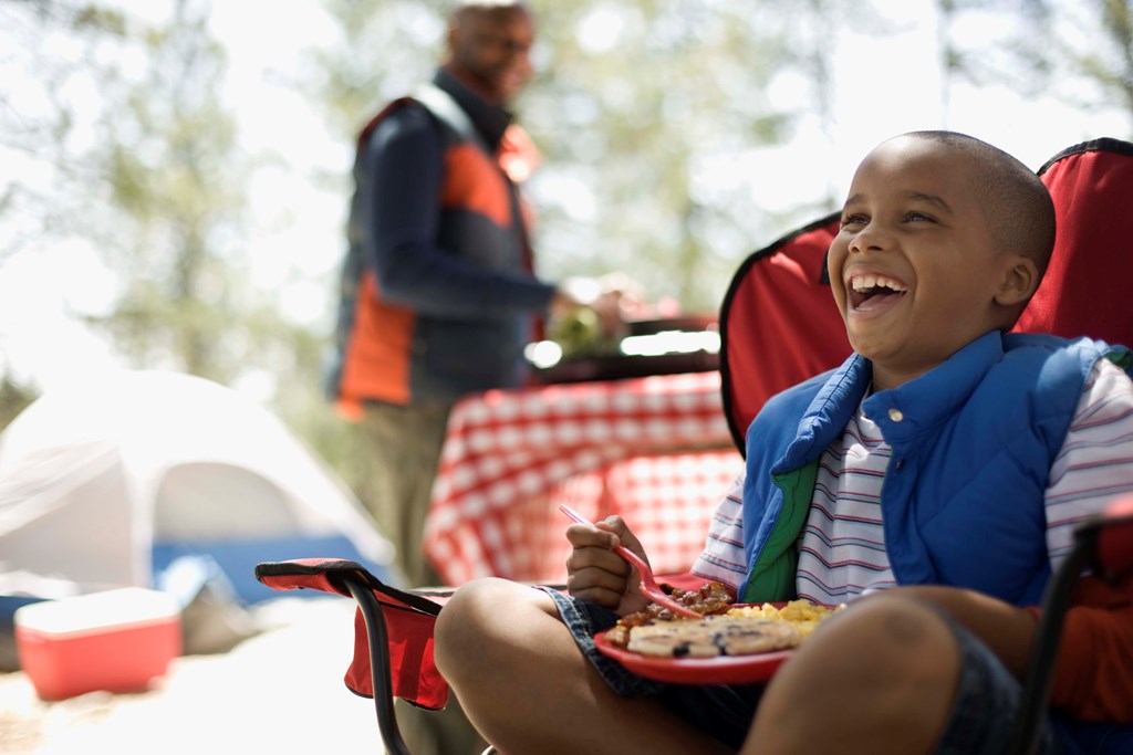 A boy laughs as he has breakfast at a KOA campsite.