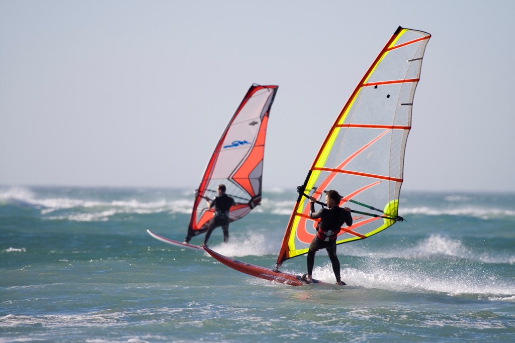 Two windsurfers in wetsuits sailing on the ocean during a bright summer's day