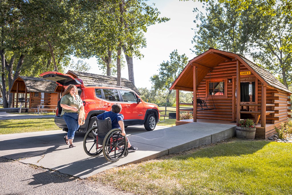 A camper in a wheelchair and his partner approach an accessible cabin with a ramp entrance.
