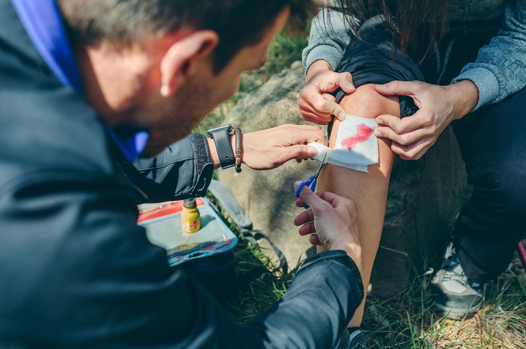 Man applying a bandage to a cut on a woman's knee during a hike.