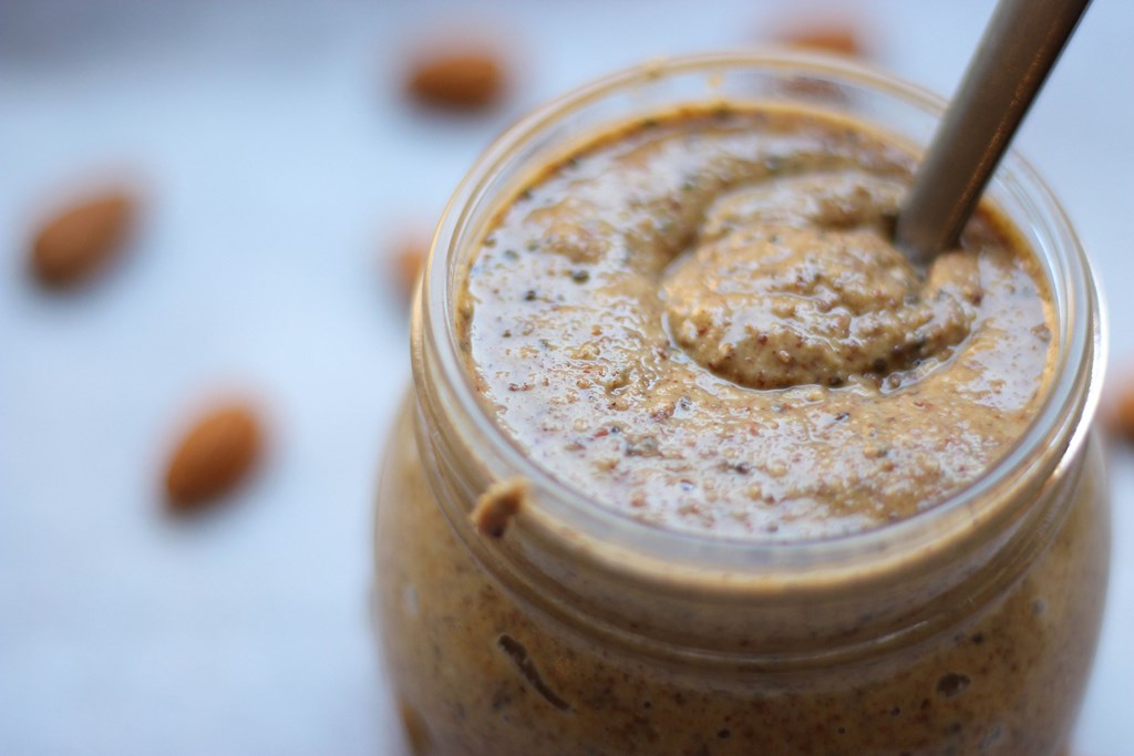 Homemade almond butter close up with wooden spoon.