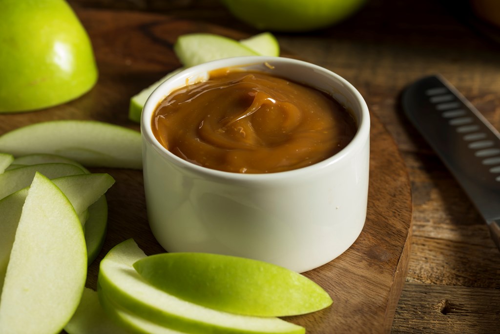 Slices of green apple with caramel dip on a wood background.
