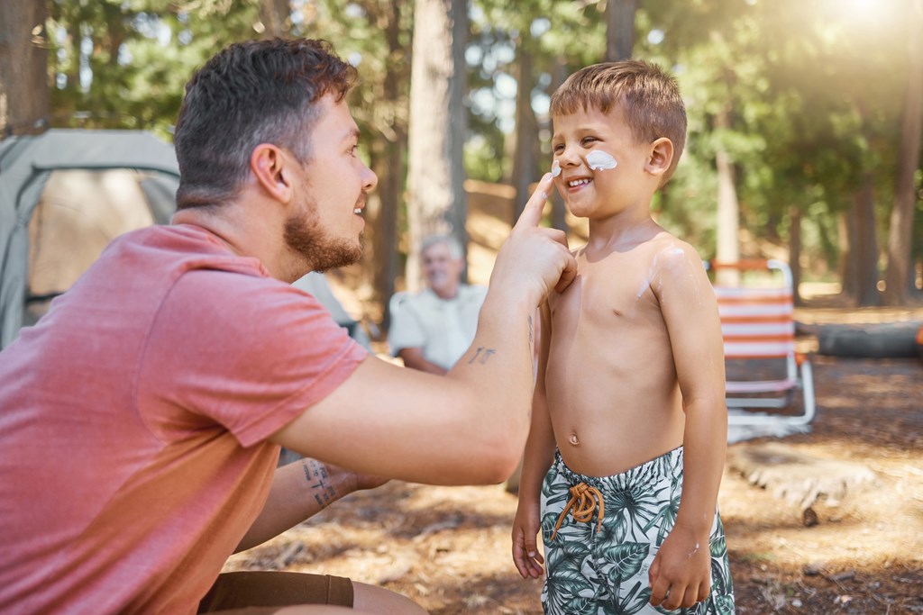 Father applying sunscreen to young boy's face on a KOA campground. 