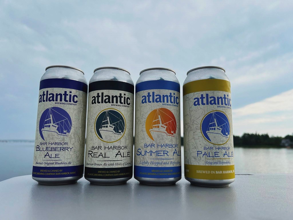 Four beer cans in front of an ocean background.