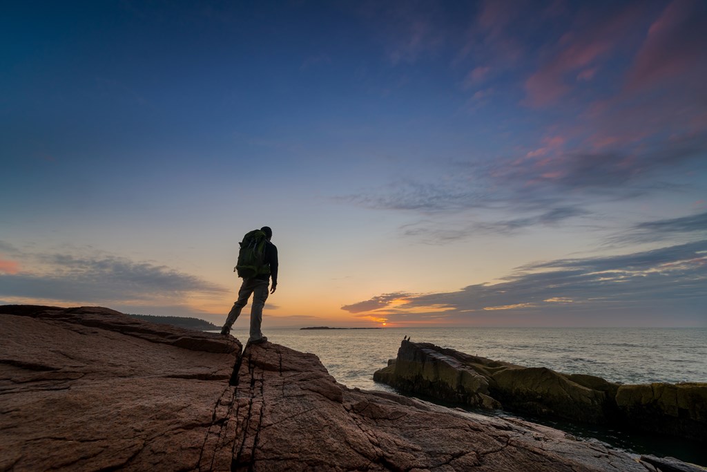 Male backpacker standing near the waters edge in Acadia National Park during a sunrise.