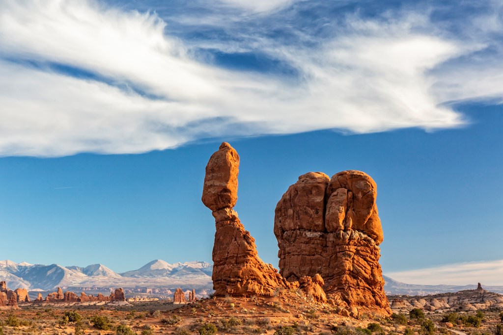 Wispy bird-like clouds over iconic Balanced Rock against the La Sal Mountain in Arches National Park in Moab, Utah.