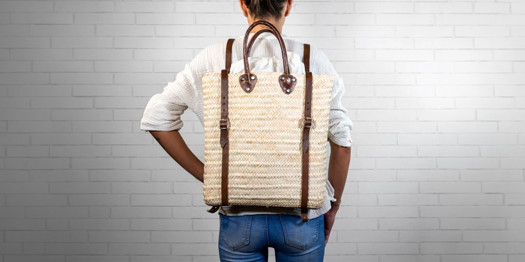 Women wearing a basket backpack on a white brick background.