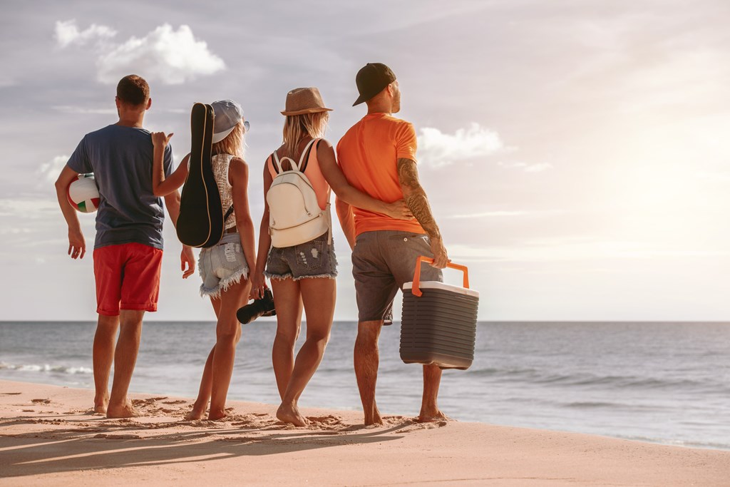 Four friends having rest at sunset picnic on sea beach