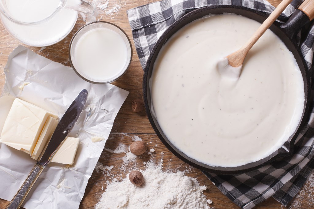 Preparation of bechamel sauce in a pan and ingredients on the table. 