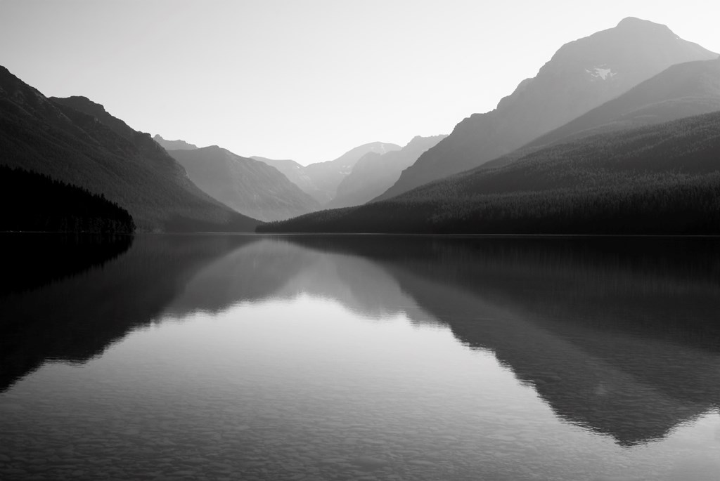 Bowman Lake in Glacier National Park. Calm, mirror-like lake surrounded by mountains in black and white.