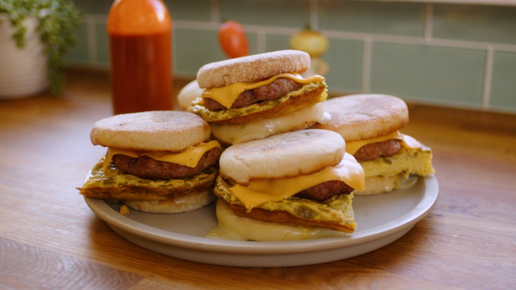 A stack of breakfast sandwiches on English muffins on a plate.