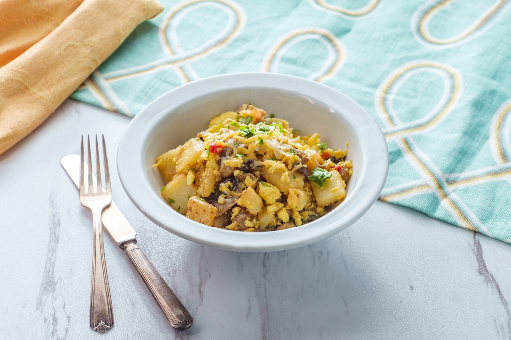 Breakfast egg scramble bowl with sausage potatoes mushrooms and cheddar cheese.