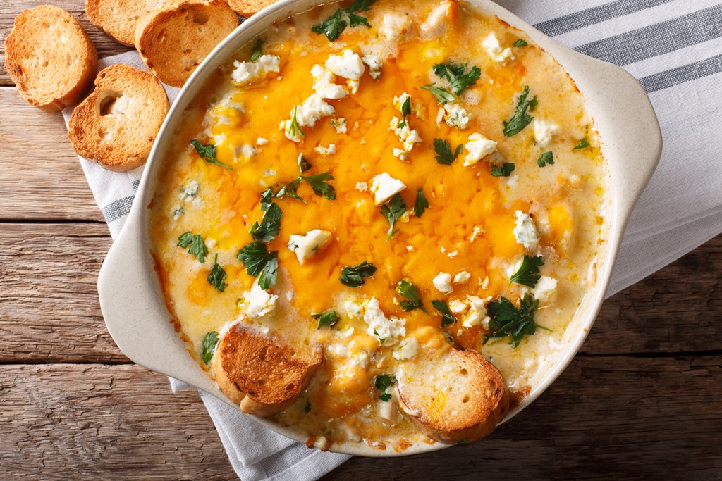 Chicken buffalo dip with blue cheese and greens close-up in a baking dish on a table. Horizontal top view from above.