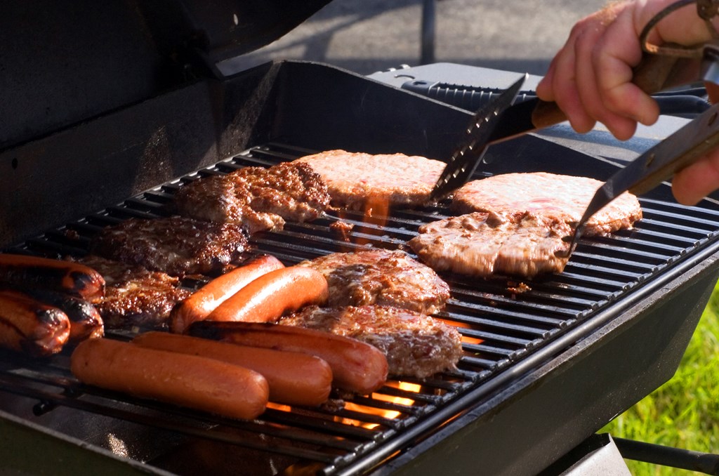 Hotdogs and hamburgers on the grill at a summer cookout.