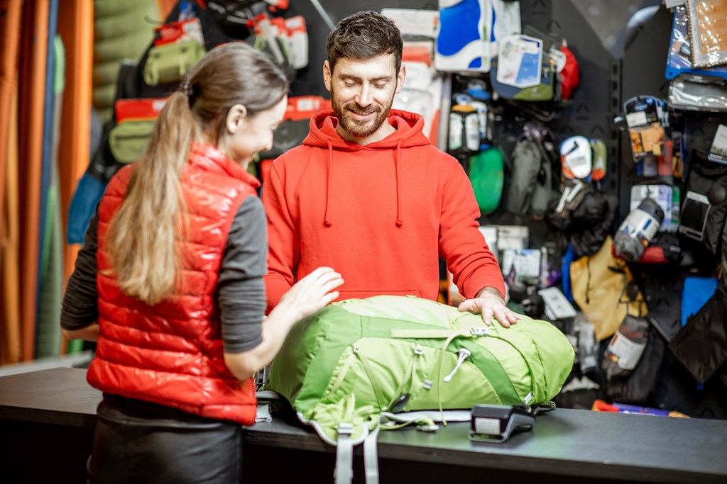 Young woman purchasing a backpack from an associate at a sporting goods store.