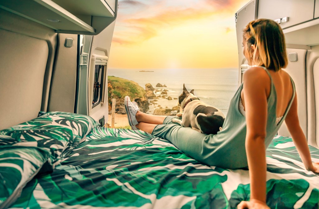 Young woman with her boston terrier dog watching the sunset sitting on the bed of her camper van.