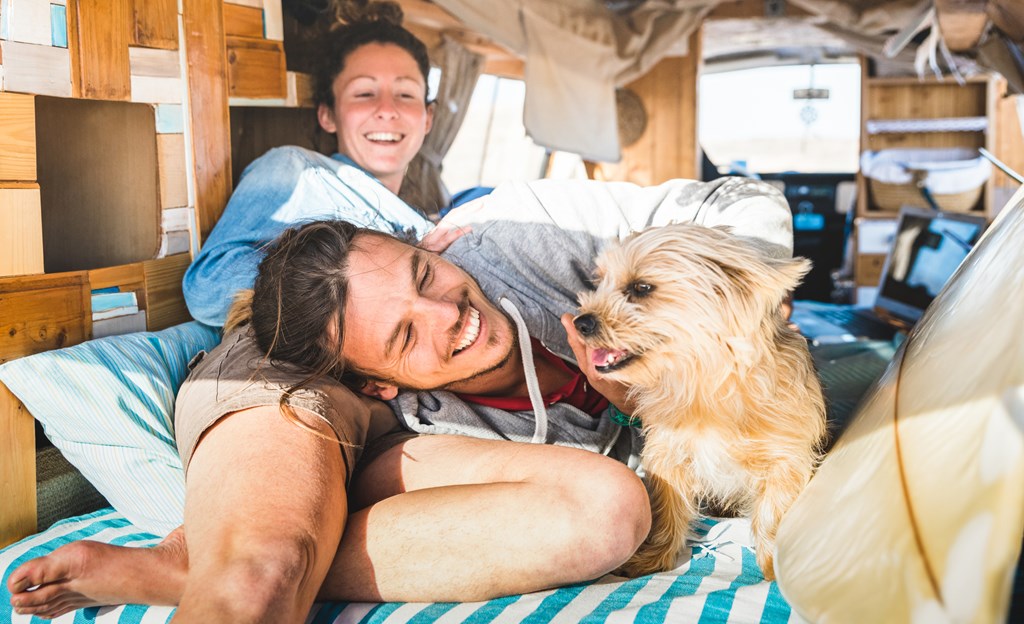 Young couple lounges in the back of a camper van with their small dog.