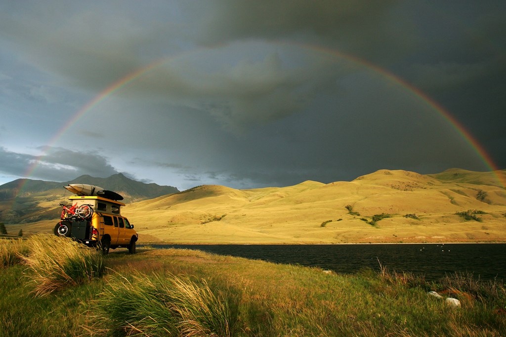 A yellow camper van parked under a rainbow.