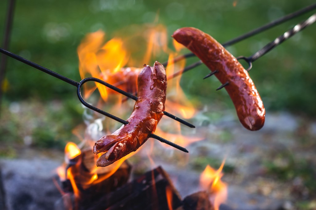 Closeup of hot dogs roasting over a campfire.