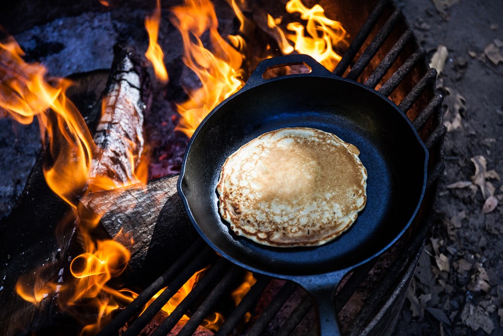 Pancake cooking in a cast iron pan over a campfire.